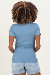 woman wearing a blue short sleeve maternity top with gathered sides, styled with denim shorts, showing her back