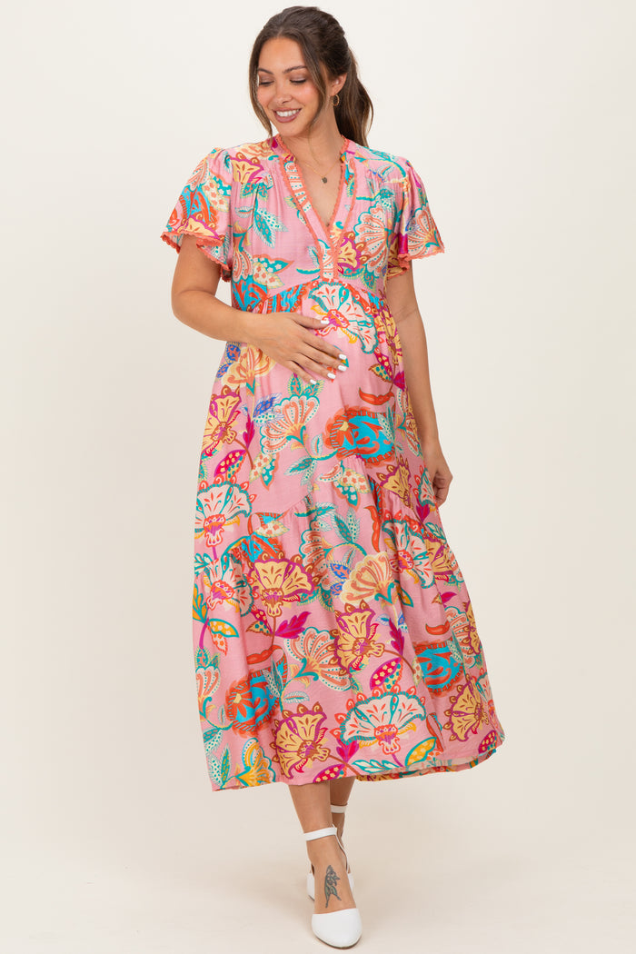 woman wearing a colorful floral print maternity dress and holding her baby bump