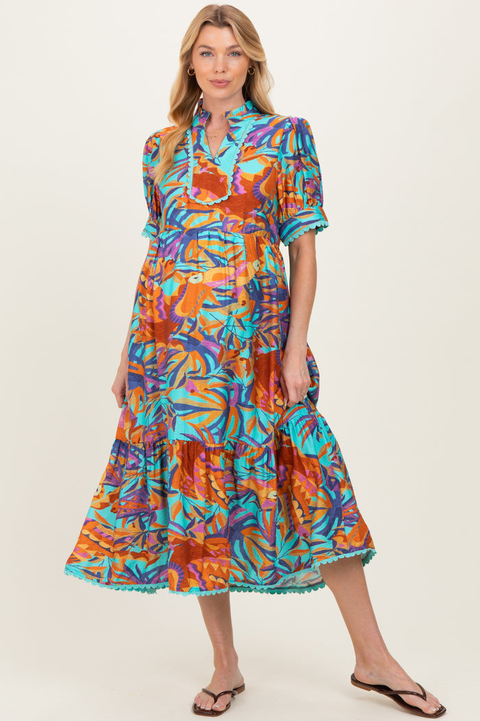 woman wearing a colorful floral print maternity dress with a tiered skirt and short sleeves, displaying a baby bump
