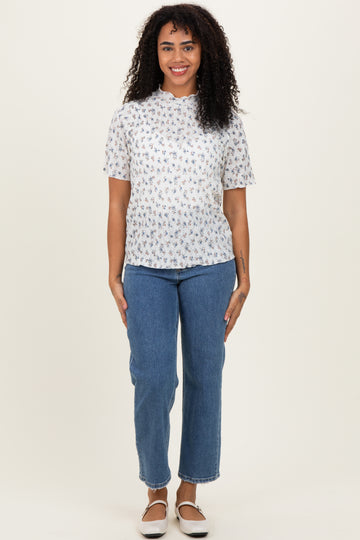 woman wearing a white short sleeve floral print top and blue high-waisted jeans standing against a neutral background
