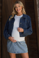 woman wearing a navy blue denim maternity jacket over a white top and a denim skirt, holding her baby bump