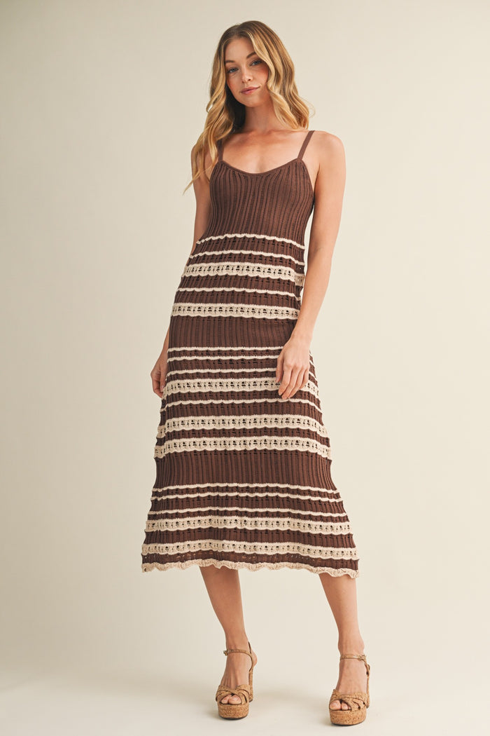 woman wearing a brown and cream striped midi dress with spaghetti straps and a tiered hem, standing in a neutral background