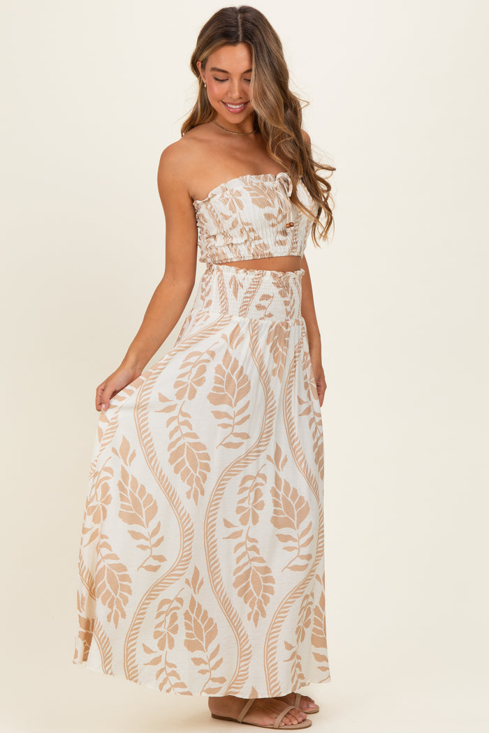 woman wearing a strapless beige and white maxi dress with a leaf pattern and a smocked waistband