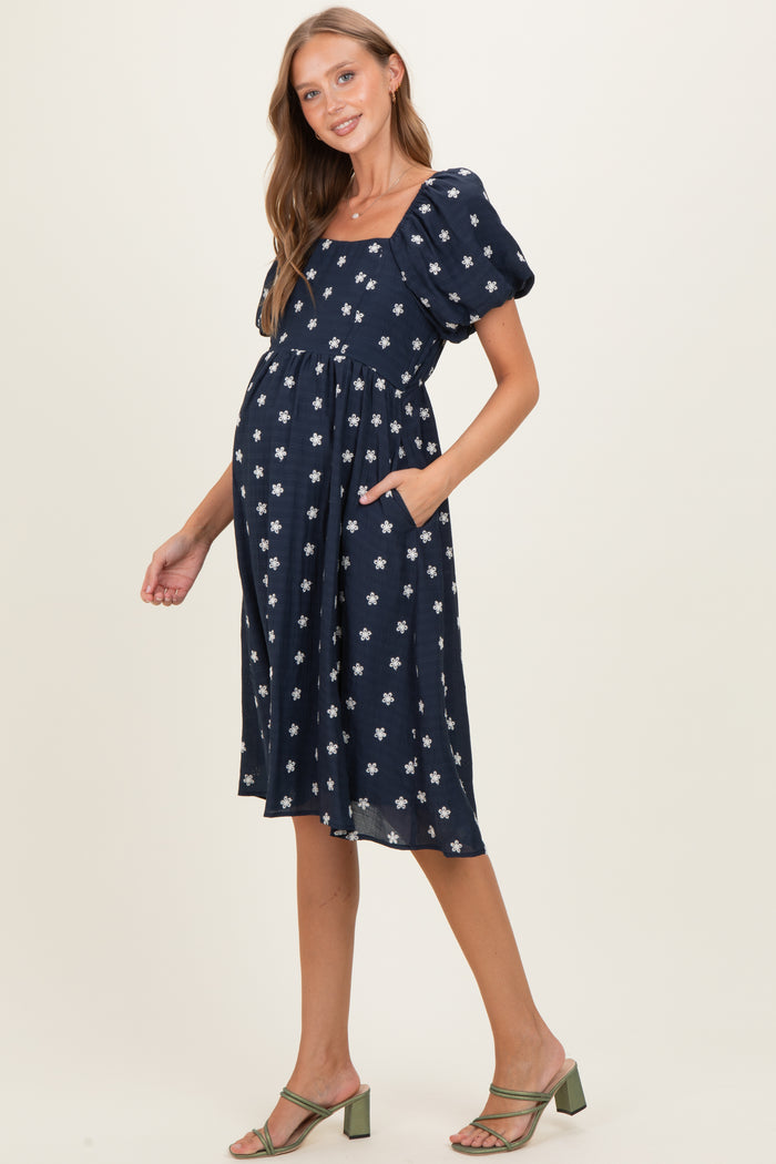woman wearing a navy blue maternity dress with puff sleeves and white floral print, showing her baby bump