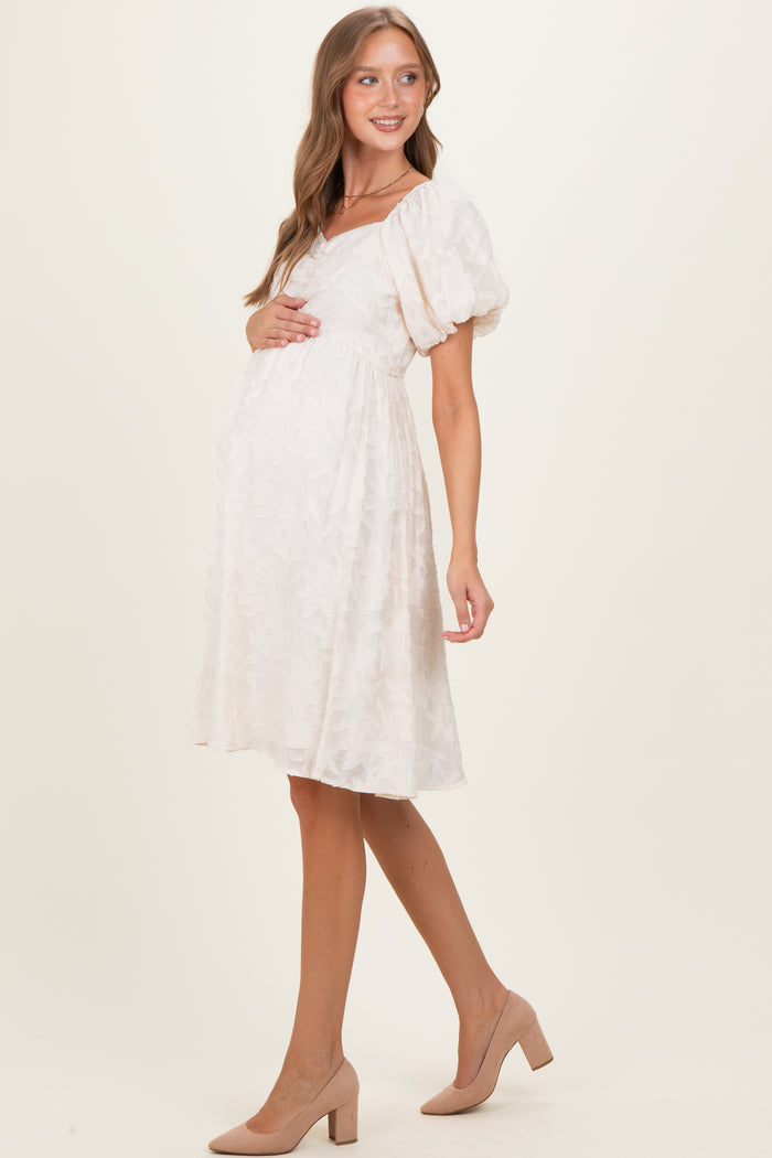 woman wearing a light pink maternity dress with puff sleeves and a fitted bodice, holding her baby bump