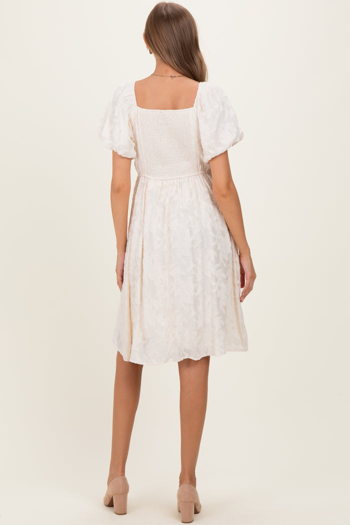 woman wearing a white floral maternity dress with puff sleeves and a fitted waist, showing her baby bump from the back