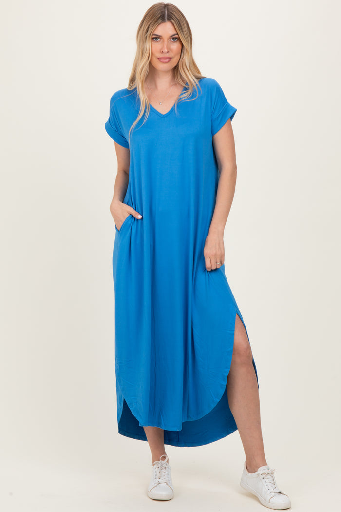 woman wearing a bright blue short sleeve maxi dress with side pockets and side slits, poses with one hand in pocket