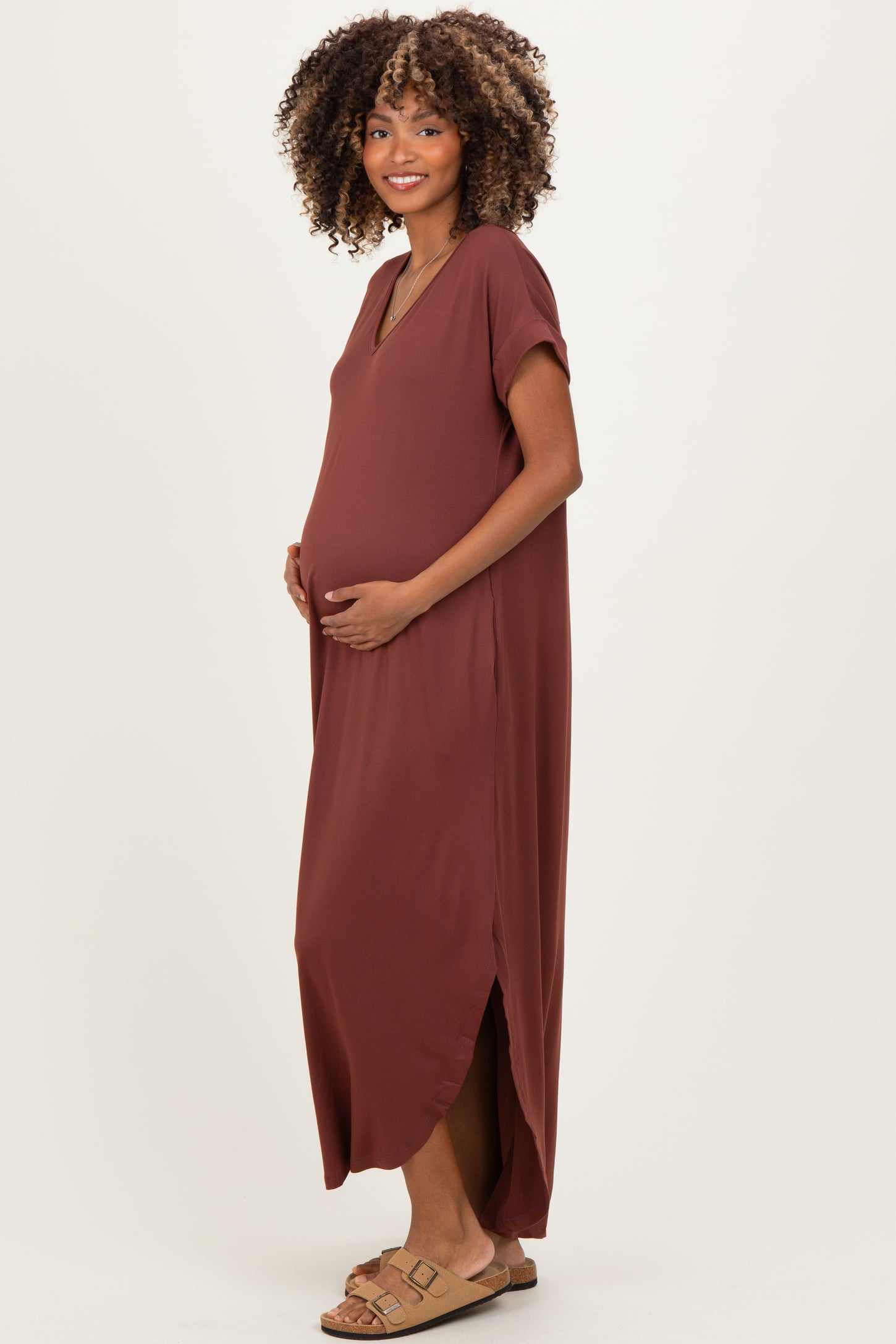 woman wearing a rust colored maternity maxi dress with a side slit and holding her baby bump