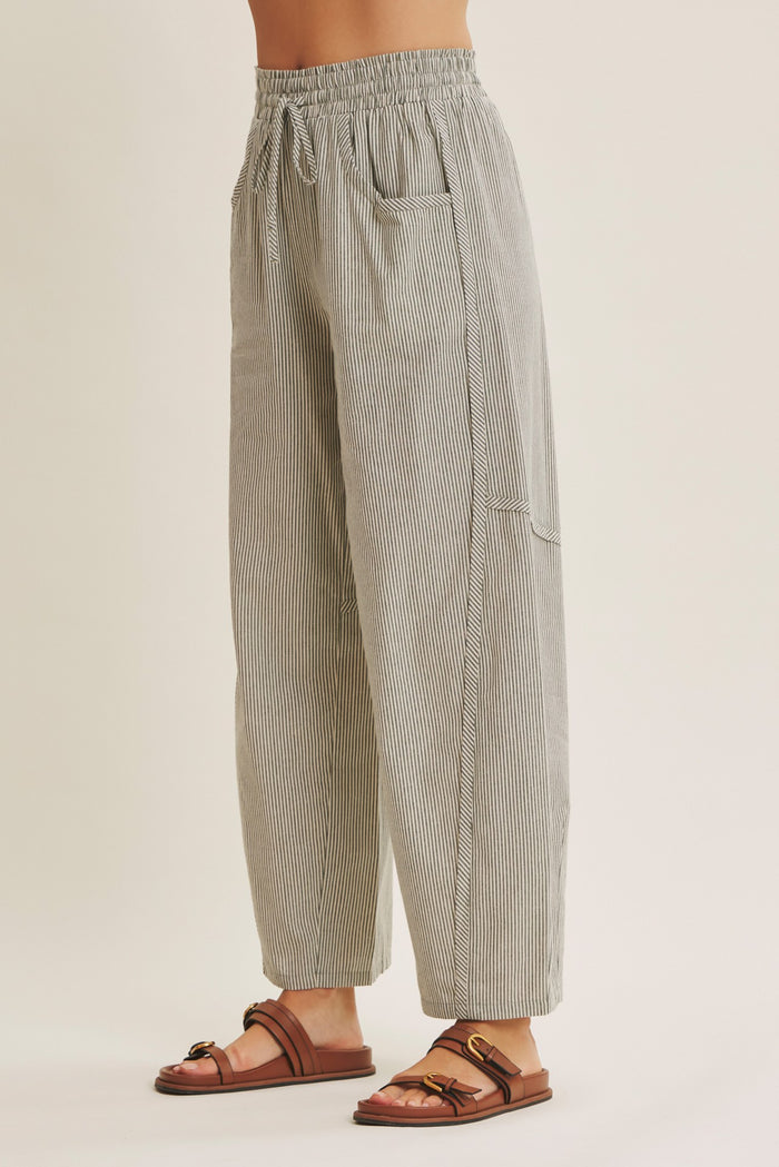 woman wearing black and white striped relaxed fit pants with elastic waistband and side pockets paired with brown sandals