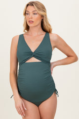 woman wearing a dark green maternity swimsuit with a twisted front and adjustable side ties, showcasing a baby bump