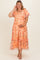 woman in a flowy peach floral maternity dress with puff sleeves and ruffled hem, gently holding her baby bump
