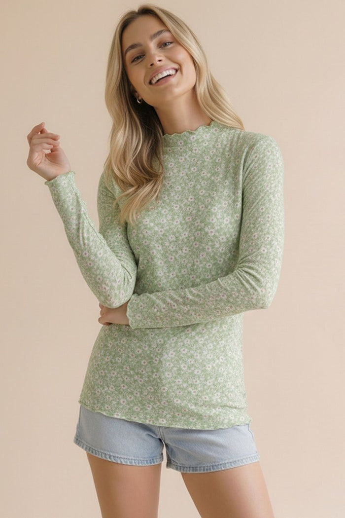 woman wearing a green long sleeve floral top with a scalloped neckline and light blue denim shorts