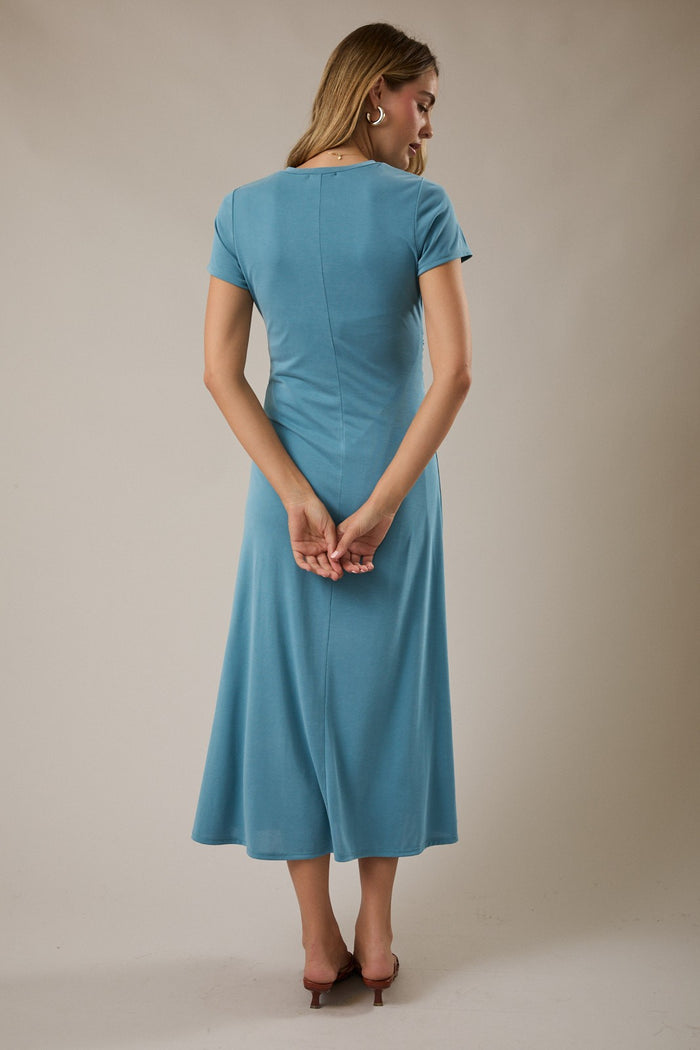 woman wearing a short sleeve blue midi dress, facing away with her hands behind her back