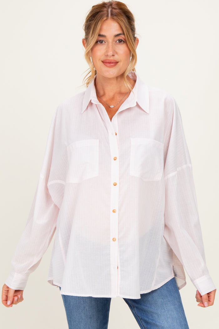 woman wearing a light pink oversized maternity shirt with buttons and breast pockets, styled with blue jeans