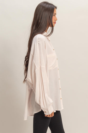 woman wearing a light pink oversized button-up shirt with long sleeves and dropped shoulders, paired with black leggings