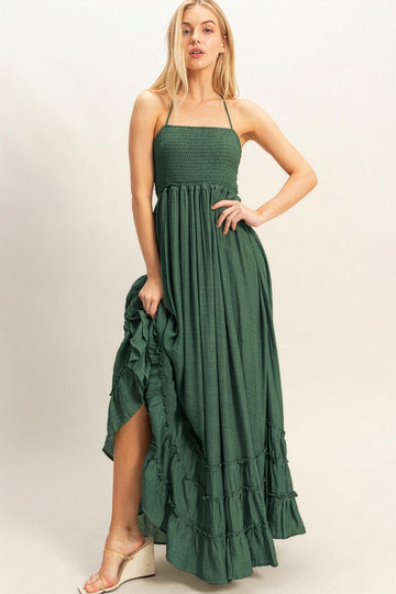 woman wearing a green maxi dress with a smocked bodice and ruffled hem, standing with one hand on her hip