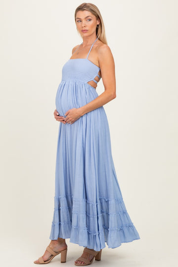 woman wearing a light blue maternity maxi dress with a smocked bodice and ruffled hem, holding her baby bump
