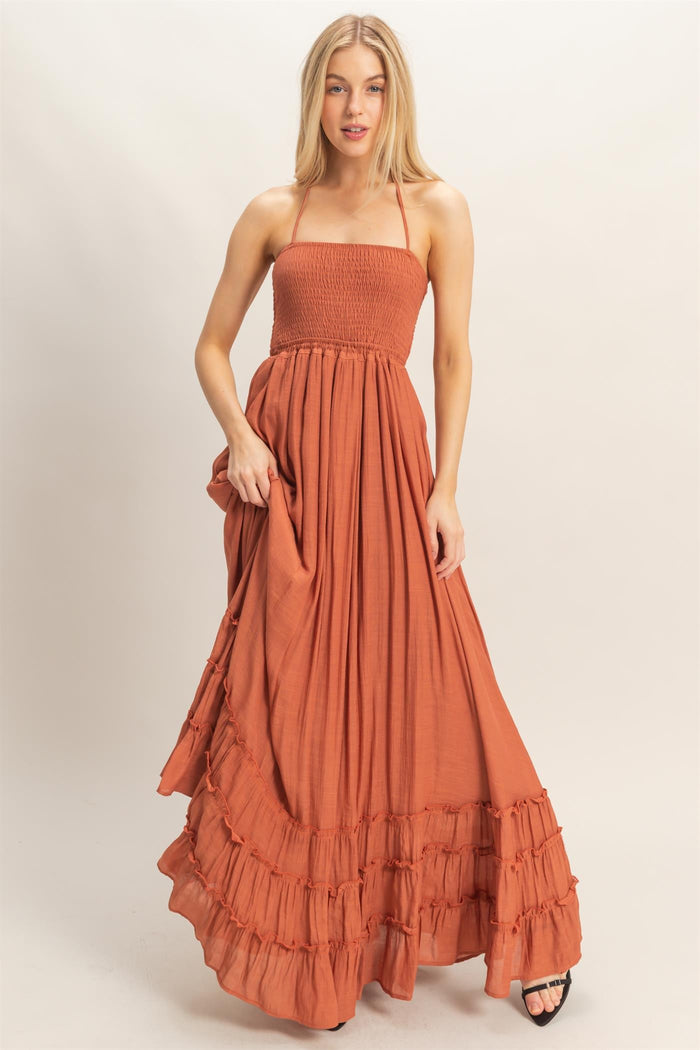 woman wearing a rust-colored strapless maxi dress with smocked bodice and ruffled hem