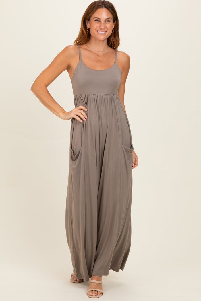 woman wearing a taupe sleeveless maxi dress with a fitted bodice and loose skirt featuring side pockets