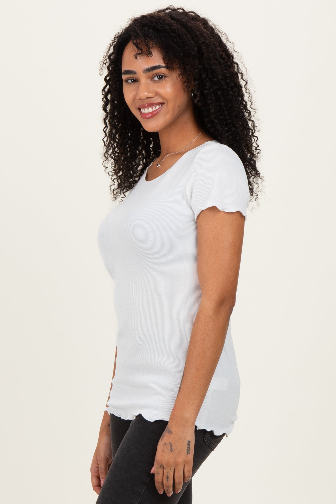 woman wearing a white ribbed top with scalloped sleeves and a fitted silhouette