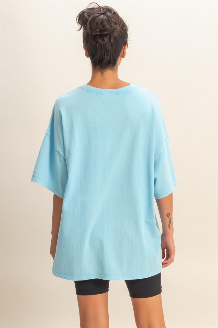 woman wearing an oversized light blue t-shirt from the back with rolled sleeves and black bike shorts
