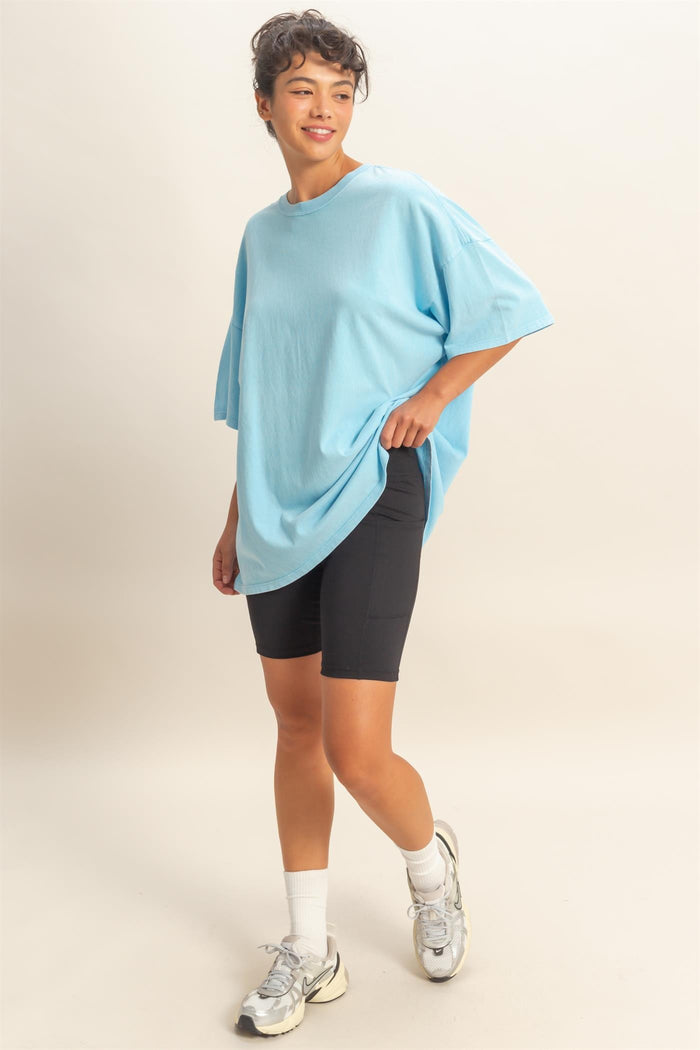 woman wearing an oversized light blue t-shirt and black bicycle shorts, posing with one hand in her pocket
