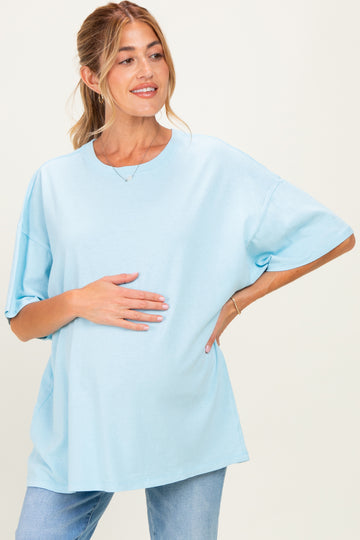 woman wearing a light blue oversized maternity t-shirt and holding her baby bump with a smile