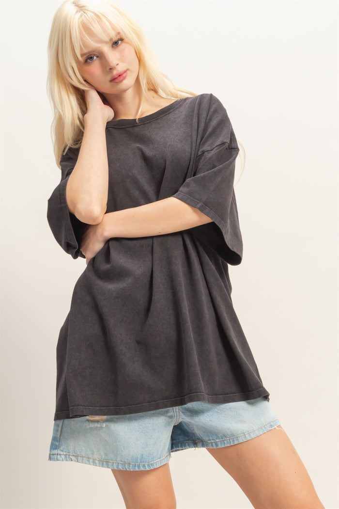 woman wearing an oversized black t-shirt and light blue denim shorts, posing with one arm crossed over her body