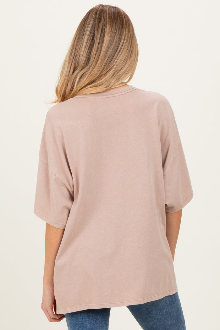 woman wearing a loose-fit light brown maternity t-shirt, seen from the back, styled with blue jeans