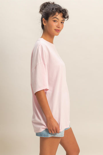 woman wearing a pastel pink oversized t-shirt with short sleeves and a relaxed fit, styled with denim shorts