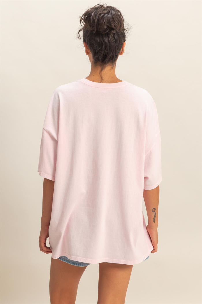 woman wearing a soft pink oversized t-shirt viewed from the back, showing a relaxed fit and rolled sleeves