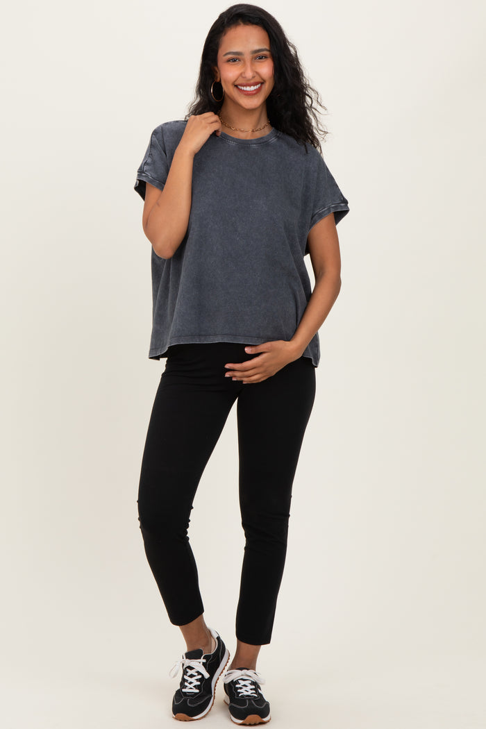 woman wearing a dark gray maternity top and black leggings, holding her baby bump