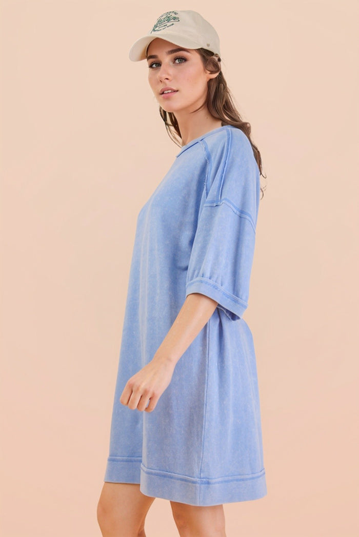 woman wearing a light blue oversized sweatshirt dress with short sleeves and a relaxed fit, styled with a beige cap
