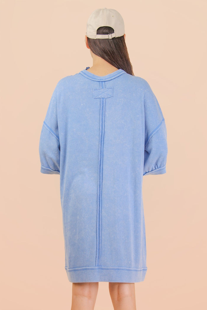 woman wearing a light blue oversized sweatshirt dress with short sleeves and a relaxed fit, seen from the back