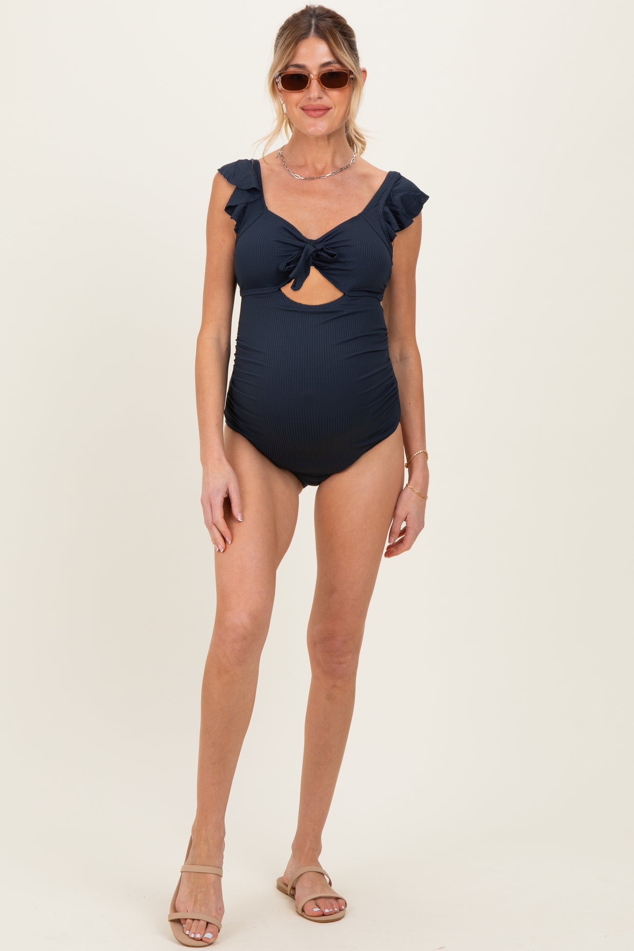 woman wearing a navy blue maternity swimsuit with ruffle sleeves and a front cutout, showing a baby bump