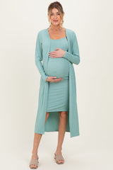 woman wearing a light teal maternity dress with ribbed texture and a matching long cardigan, holding her baby bump