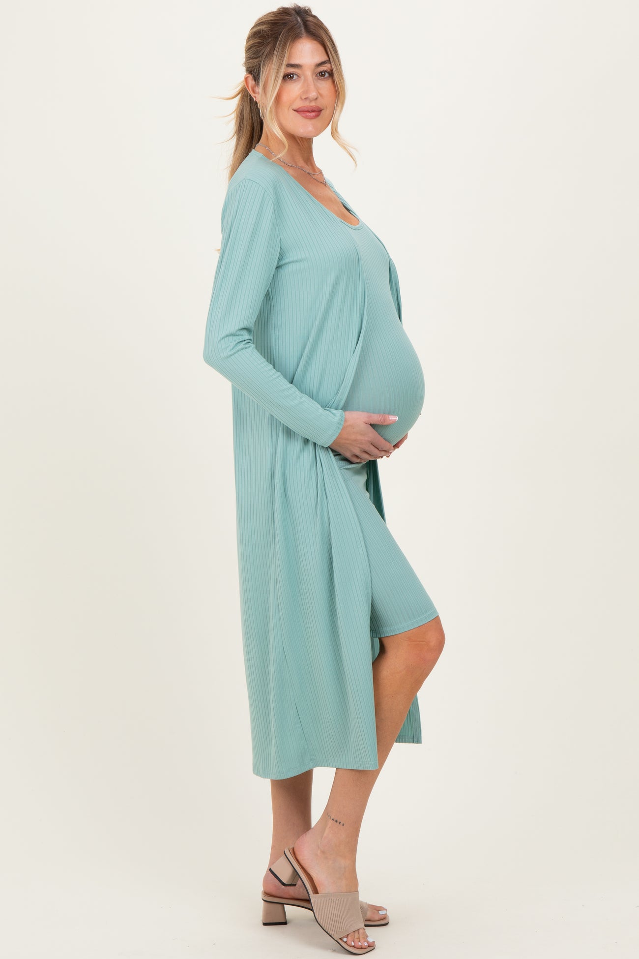 woman wearing a light teal maternity dress with a long cardigan and holding her baby bump