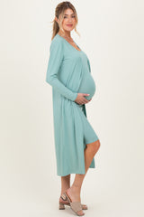 woman wearing a light teal maternity dress with a long cardigan and holding her baby bump