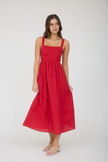 woman wearing a red sleeveless midi dress with a fitted bodice and tiered skirt, standing with one hand on her hip