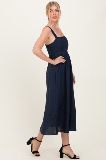 woman wearing a navy blue midi dress with spaghetti straps and a fitted waist, styled with black strappy heels