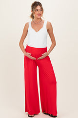 woman wearing a white maternity bodysuit and red wide-leg pants while holding her baby bump