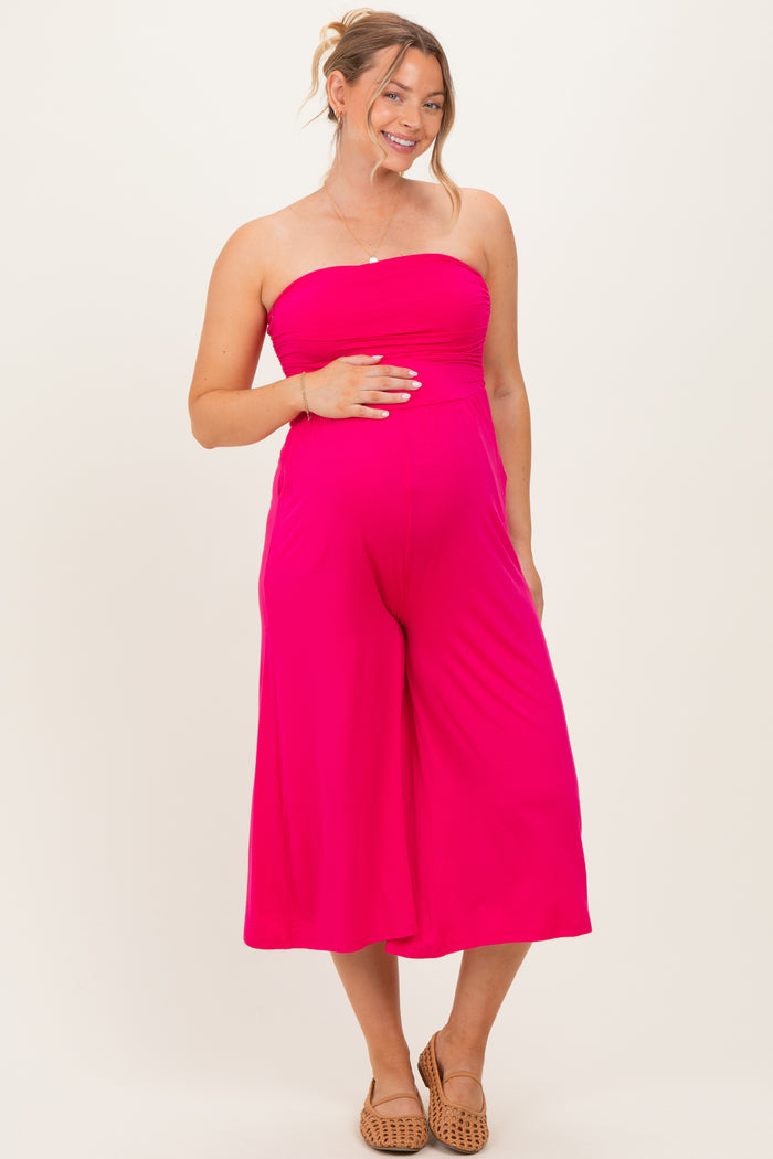 woman wearing a bright pink strapless maternity jumpsuit and holding her baby bump