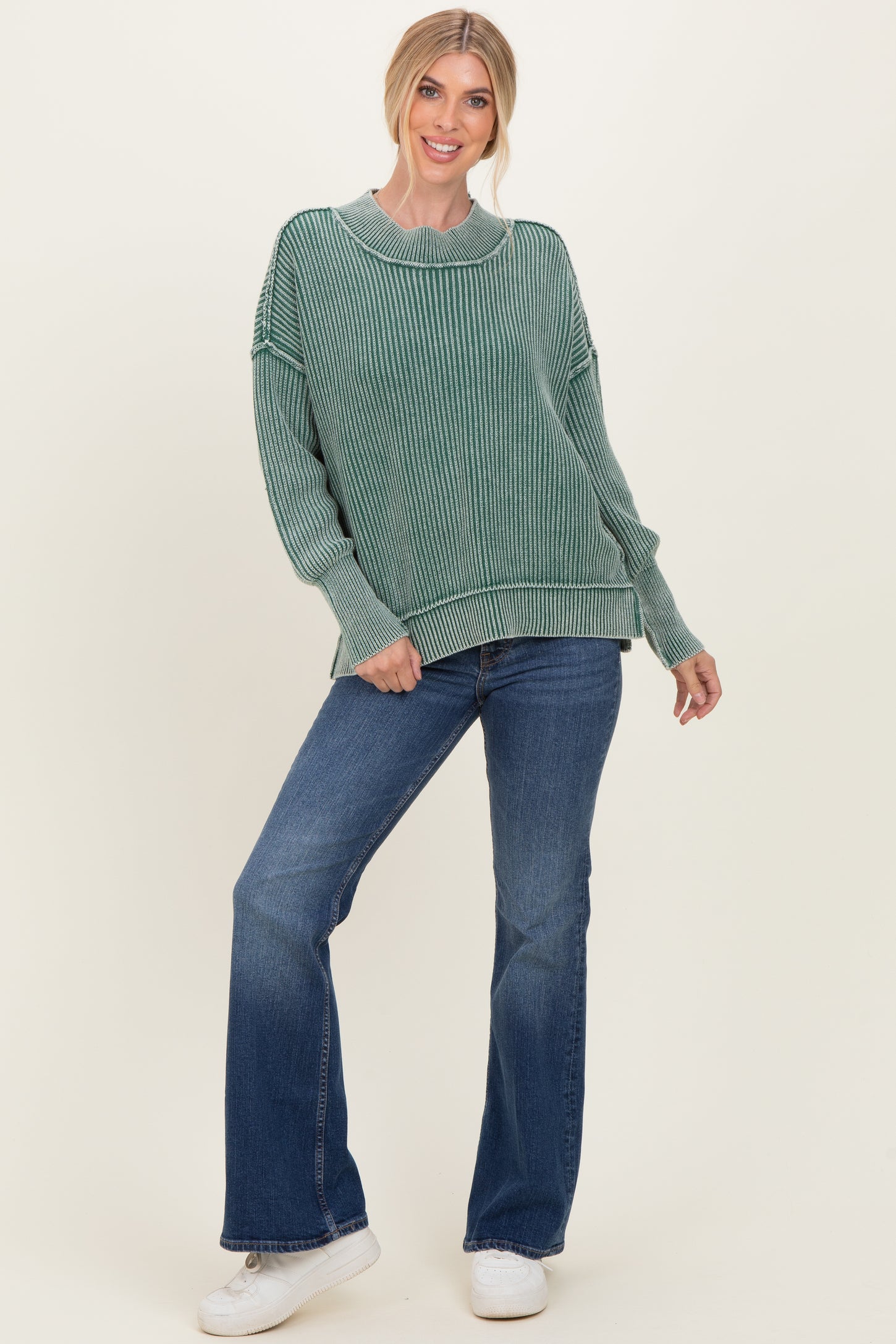 woman wearing a green striped oversized sweater and flared jeans with white sneakers