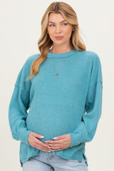 woman wearing a teal maternity sweater with ribbed texture, holding her baby bump and smiling
