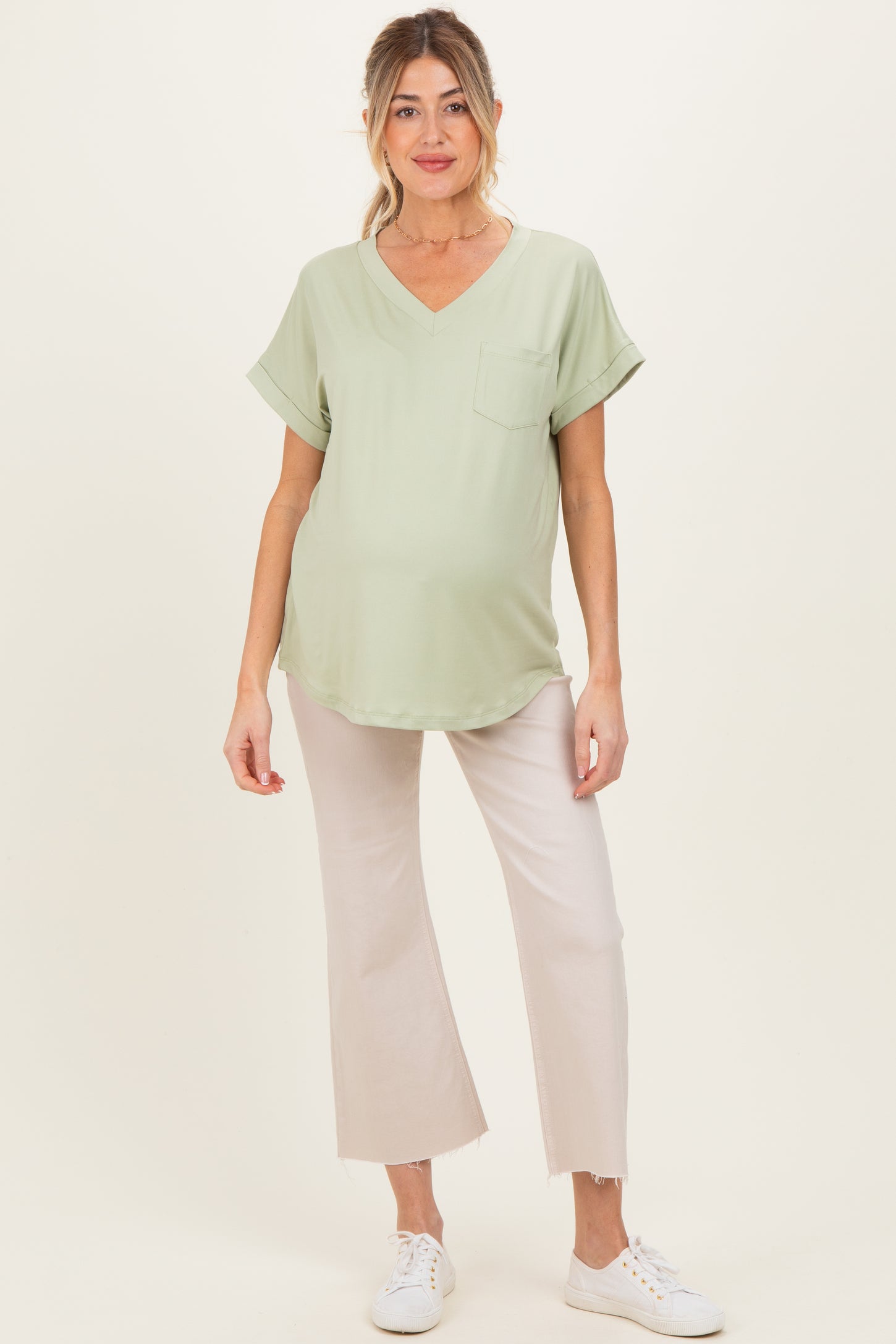 woman wearing a light green v-neck maternity top with a pocket and light beige wide-leg pants, showing her baby bump
