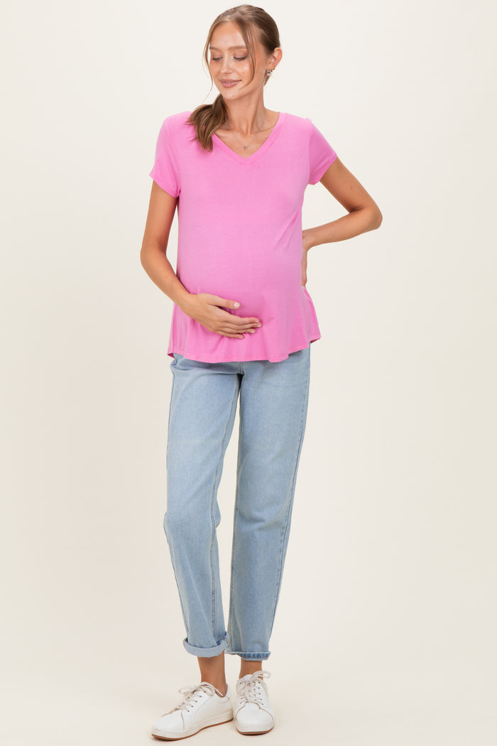 woman wearing a pink short sleeve maternity top and holding her baby bump, paired with light blue jeans