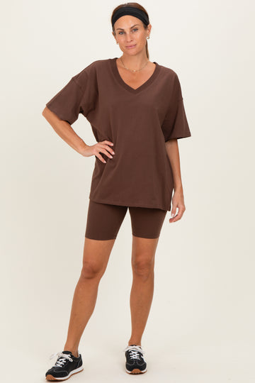 woman wearing a brown oversized v-neck t-shirt and matching bike shorts, standing in a casual pose