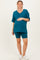 woman wearing a teal maternity t-shirt and matching bike shorts, gently holding her baby bump