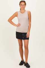 woman wearing a beige ribbed sleeveless top and a black denim mini skirt with buttons