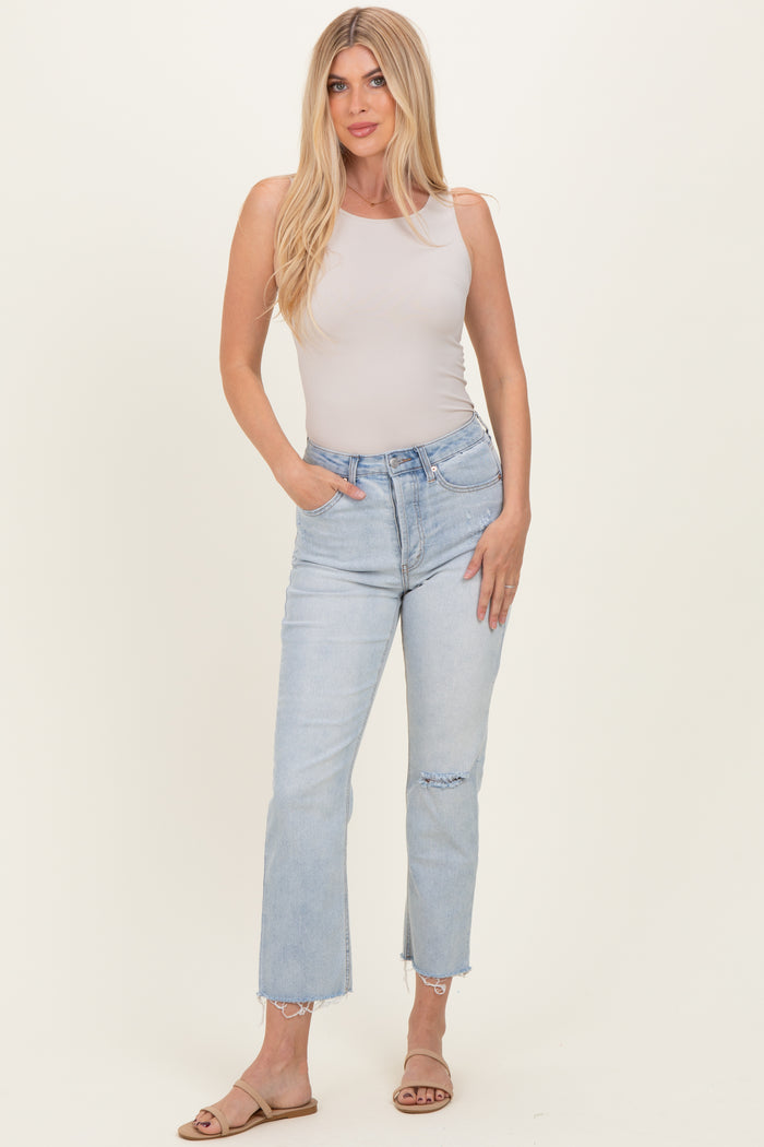woman wearing a light beige sleeveless bodysuit and light blue straight leg jeans with a distressed hem